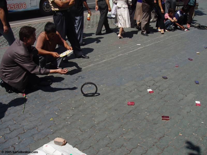 Men roll small tires to encircle and win packs of cigarettes in a street game in Urumqi, Xinjiang, China